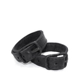 avant garde hand stitched horse culatta leather bicep belts, with an iron dye finish. the arm cuffs feature a minimal silhouette with tonal japanese linen stitching and hand forged iron buckle hardware. the arm belts are available to buy online from artisanal designer atelierskn.com 