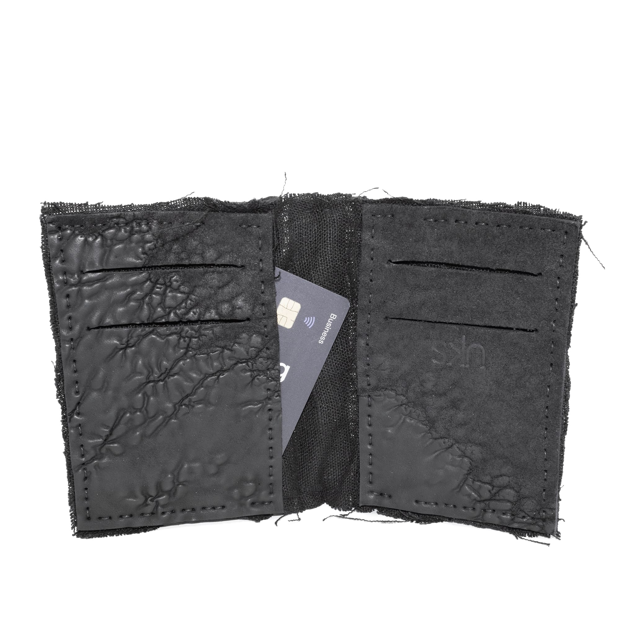 object dyed matte black reverse horse culatta leather cardholder, hand stitched over an 18 hour period without the use of machines. the leather bifold card case features multiple card slots, and a french linen lining. an open seam construction is hand stitched in a japanese linen thread. the wallet is available to buy online from avant garde leather studio atelierskn.com